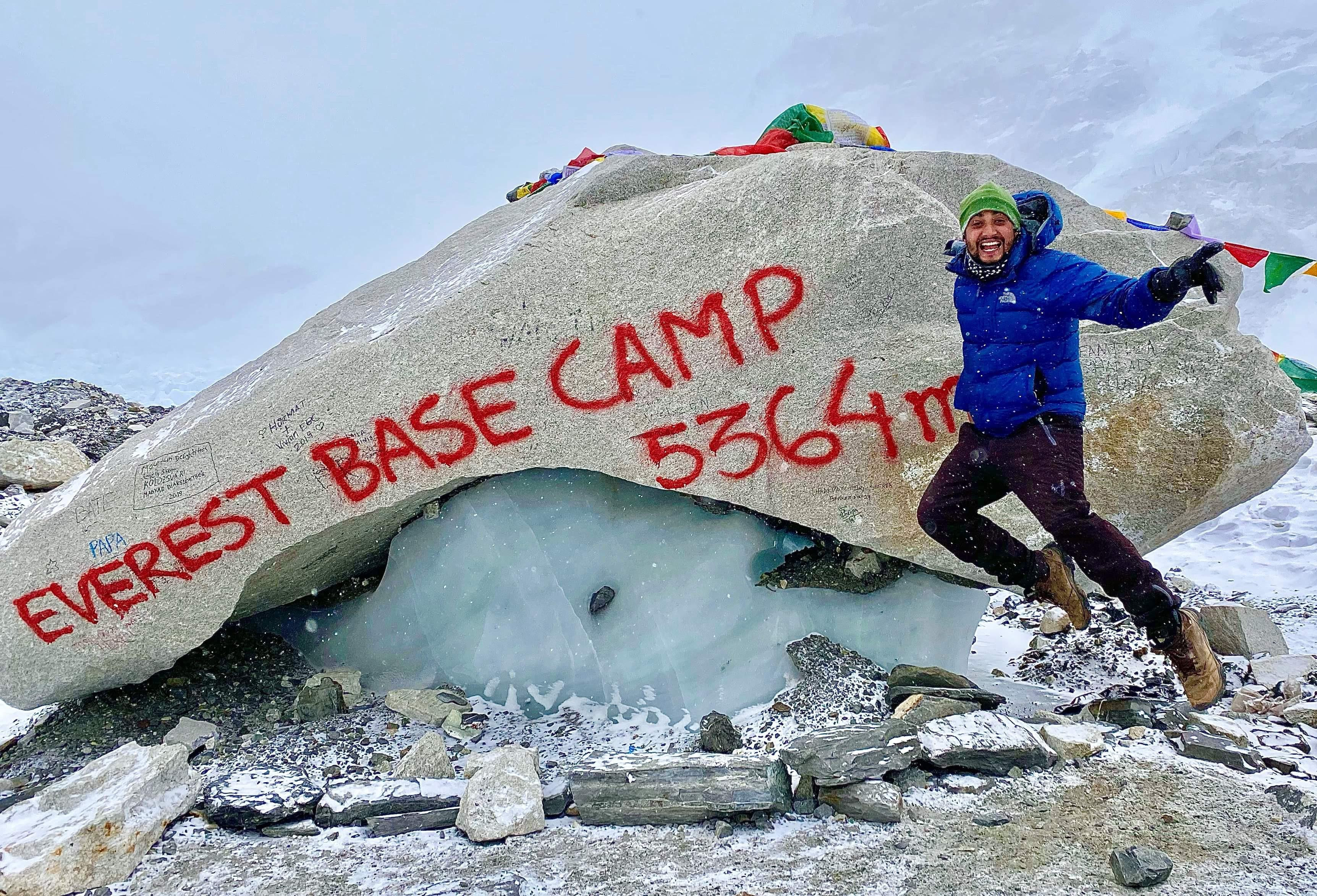a hiker jumping and posing in front of Everest Base Camp marker rock